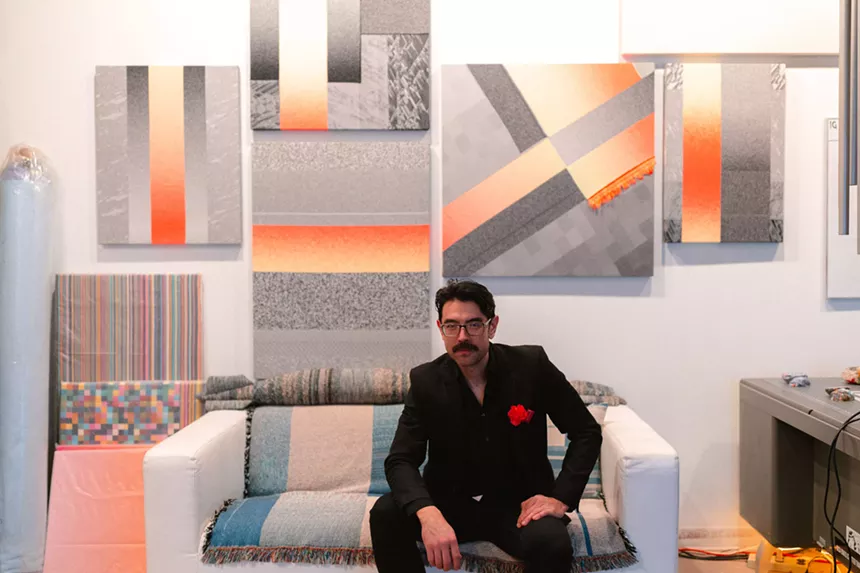 A man dressed in a suit sits on a couch beneath artwork.