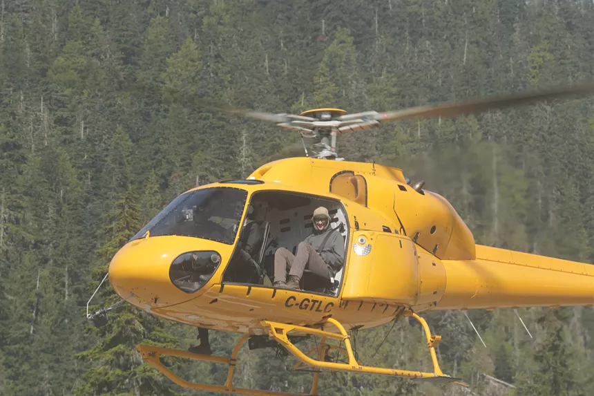 Ryan Willis seated inside a yellow helicopter with evergreen forest in the backdrop