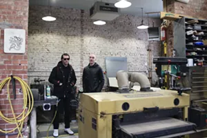 Two men stand in a small workshop