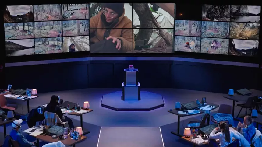 A large multi-panel screen at headquarters, picturing Hyak inside her primitive shelter