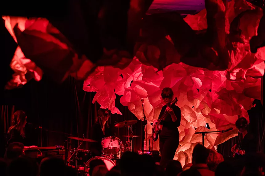 A band performs against a red background.