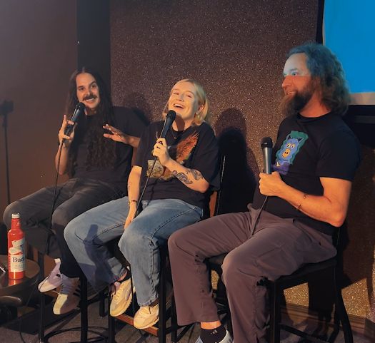 Three people sit in chairs, holding microphones in their hands.