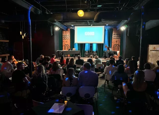 A crowded room faced a stage with a projection screen.