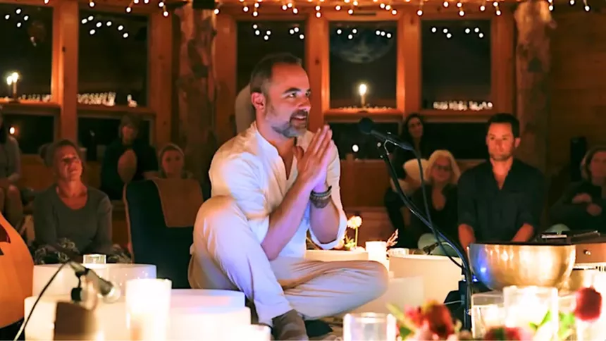 man giving prayer sign while surrounded by singing bowls