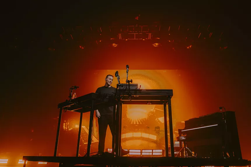 Ben Böhmer stationed at his DJ stage with a bright orange background.