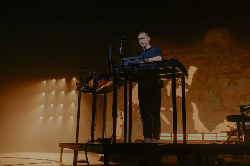 A photo of Ben Böhmer performing on stage with a production wall behind him.