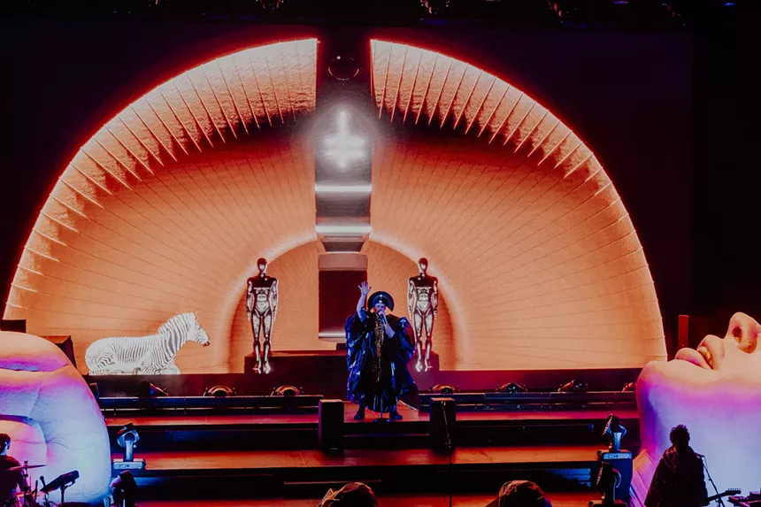 Empire of the Sun on stage with stage performers and visuals behind him.