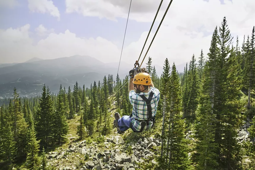 A person zipling above an evergreen forest within Breckenridge Ski Resort