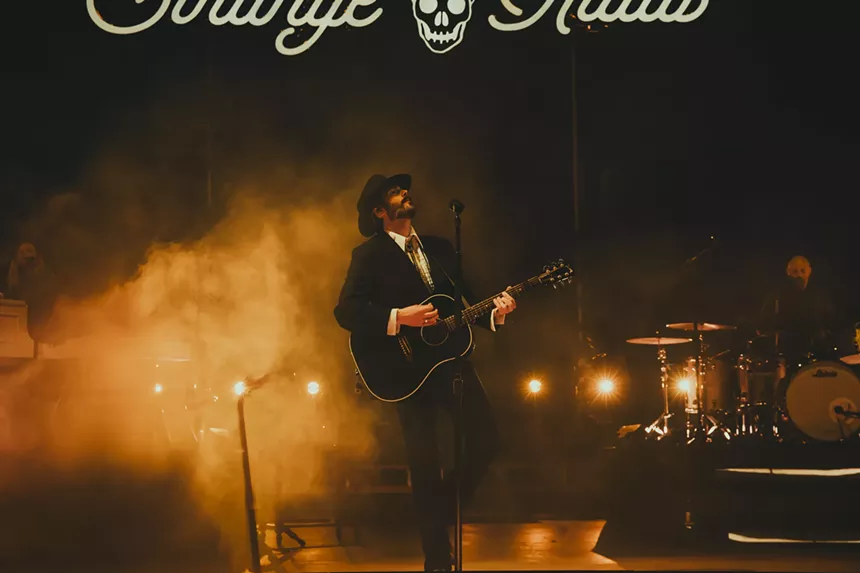 Lord Huron performing on stage at Red Rocks with fog behind him, and a stage sign labeled Strange Trails hangs above him.