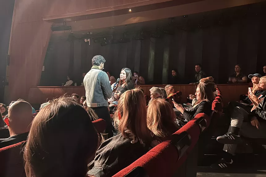 Jay Shetty holding a mic to an audience member while many others are seated in surrounding aisles