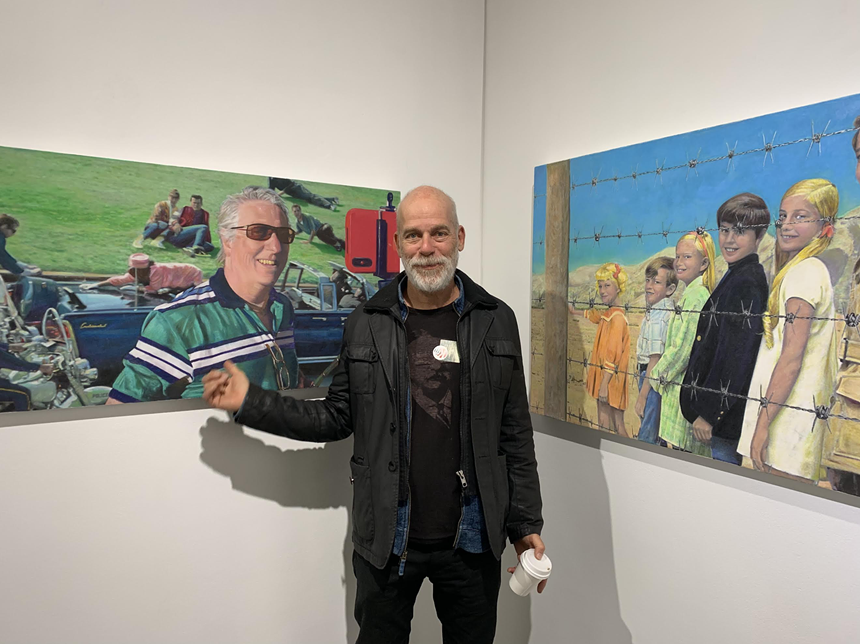 A man poses with two paintings that reimagine classic pop culture moments and characters.