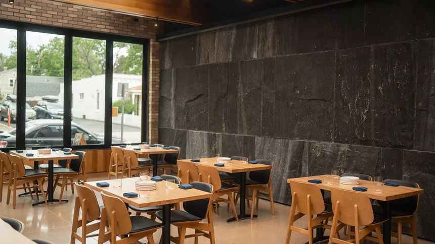 The main Denchu dining space featuring a Brazilian black limestone wall, large windows and modern wood tables and chairs