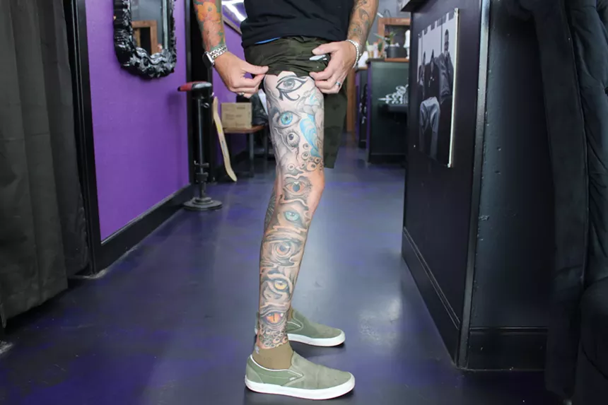 A man rolls up his pant leg to display his tattoos.
