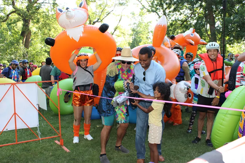 People cut a ribbon while others with inner tubes stand behind them.