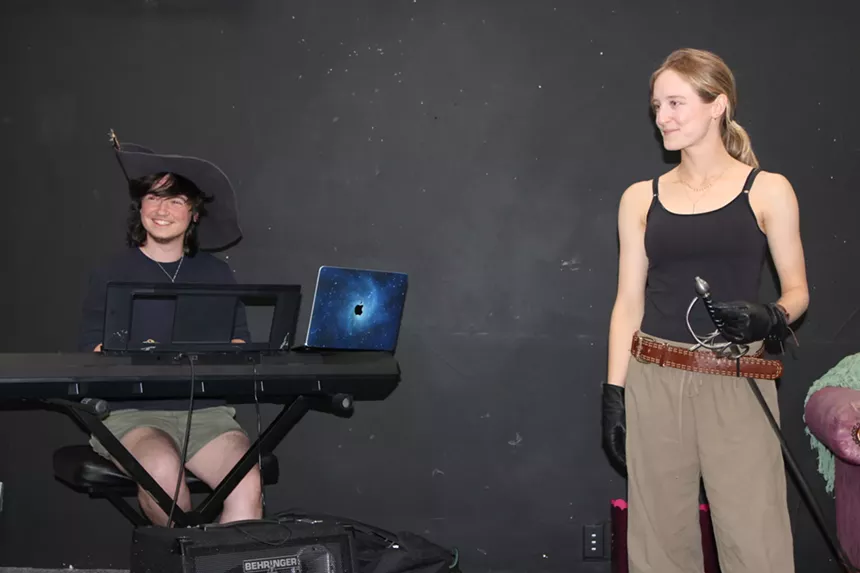 A person sits at the piano, and a woman stands next to them.