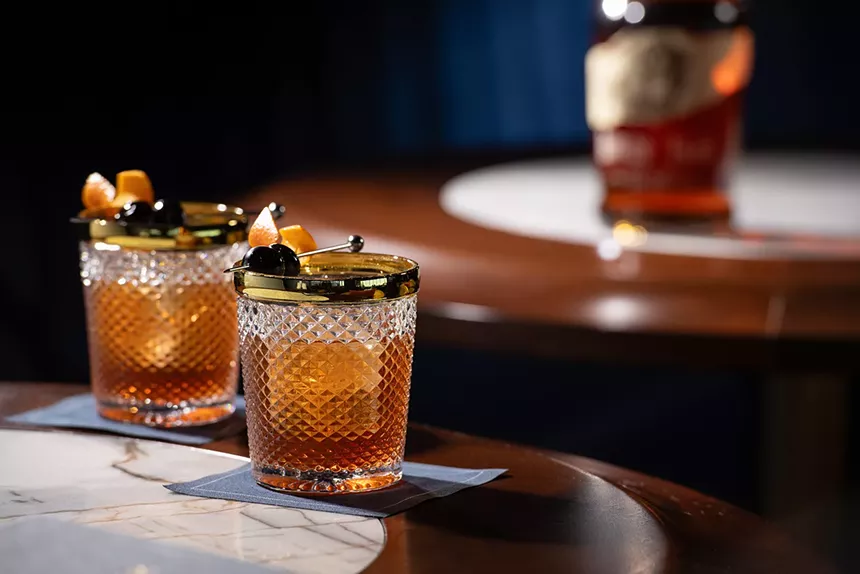 Two bourbon cocktails with orange and maraschino cherry garnishes