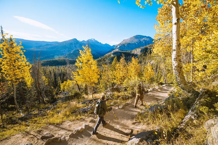 Two hikers backdropped by peaks and yellow aspens at Rocky Mountain National Park