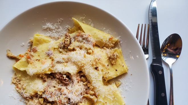 a plate of pappardelle pasta nest to a fork and knife.