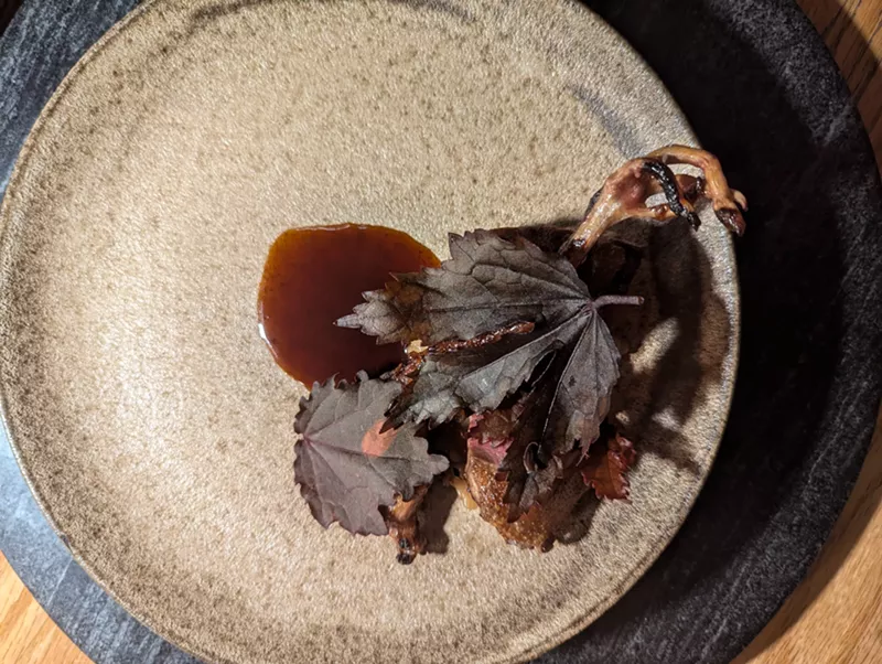 Image: leg of squab on a plate under dark purple leaves
