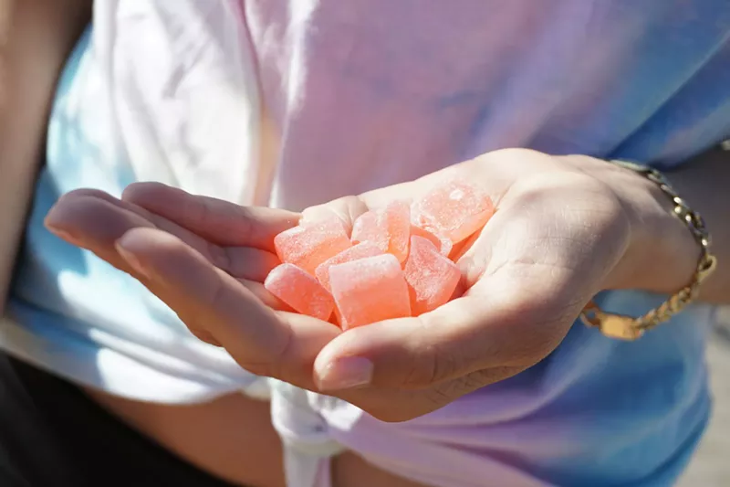 Image: Woman's hand holds orange cannabis gummies