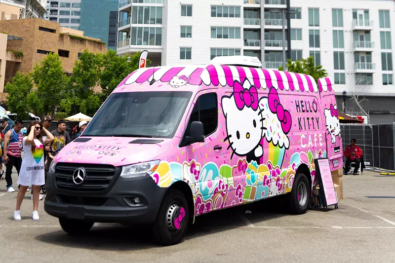 Image: A pink Hello Kitty-themed truck serves sweet treats and drinks to customers on a sunny day.