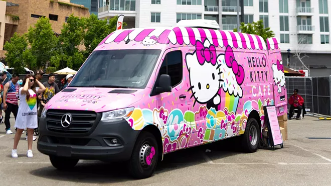 A pink Hello Kitty-themed truck serves sweet treats and drinks to customers on a sunny day.