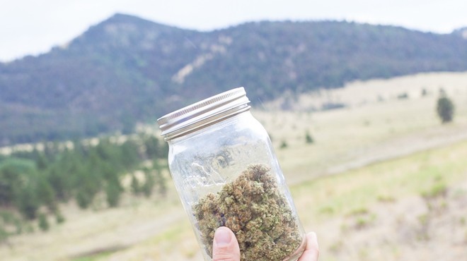 A jar of marijuana held in front of Colorado mountains