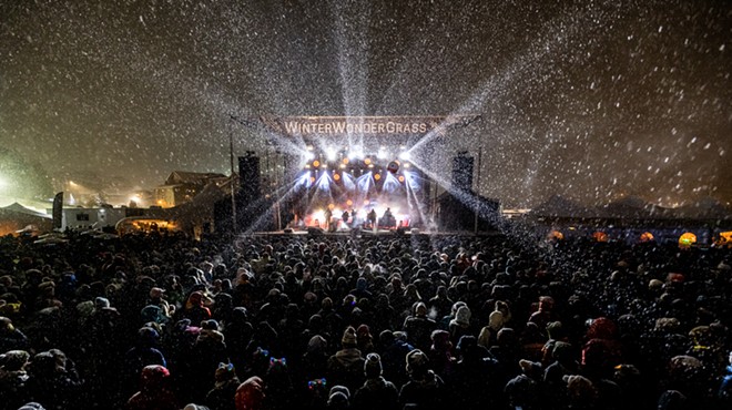 a stage with the words WinterWonderGrass is surrounded by an audience in the snow