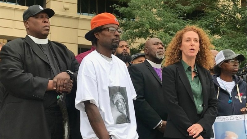 Attorney Mari Newman speaking at an October 1, 2020, press conference about the death of Elijah McClain while flanked by his father, Lawayne Mosley (in orange cap), and his mother, Sheneen McClain (far right).